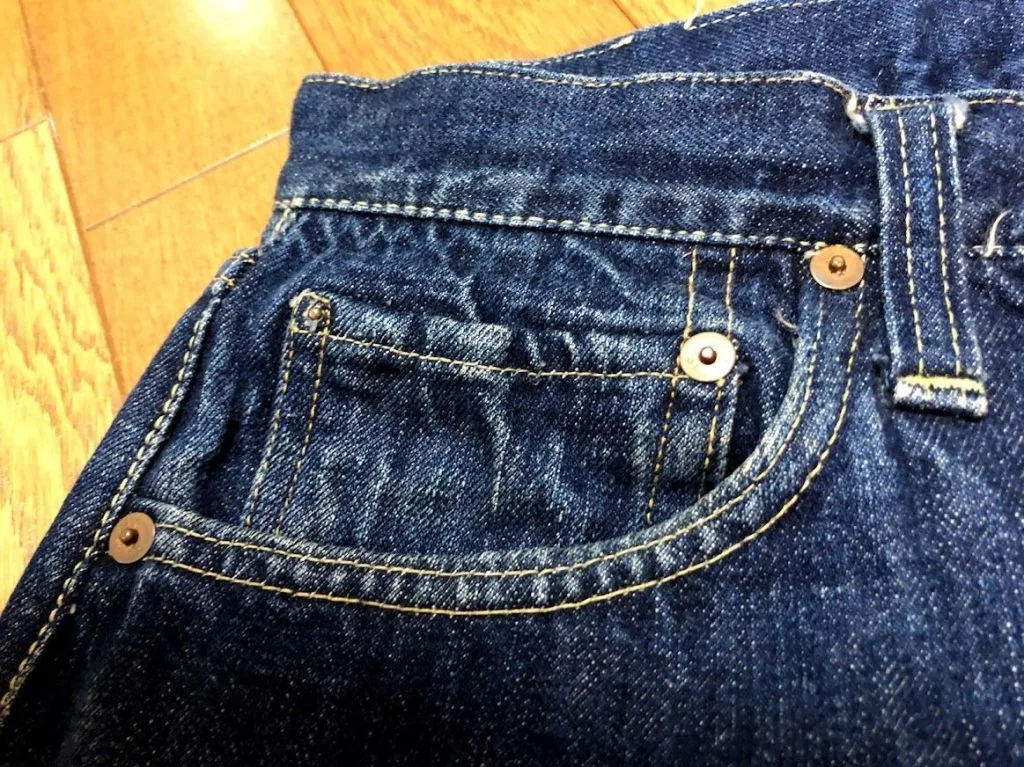 Qual é a função do pino de metal nas laterais da calça jeans?